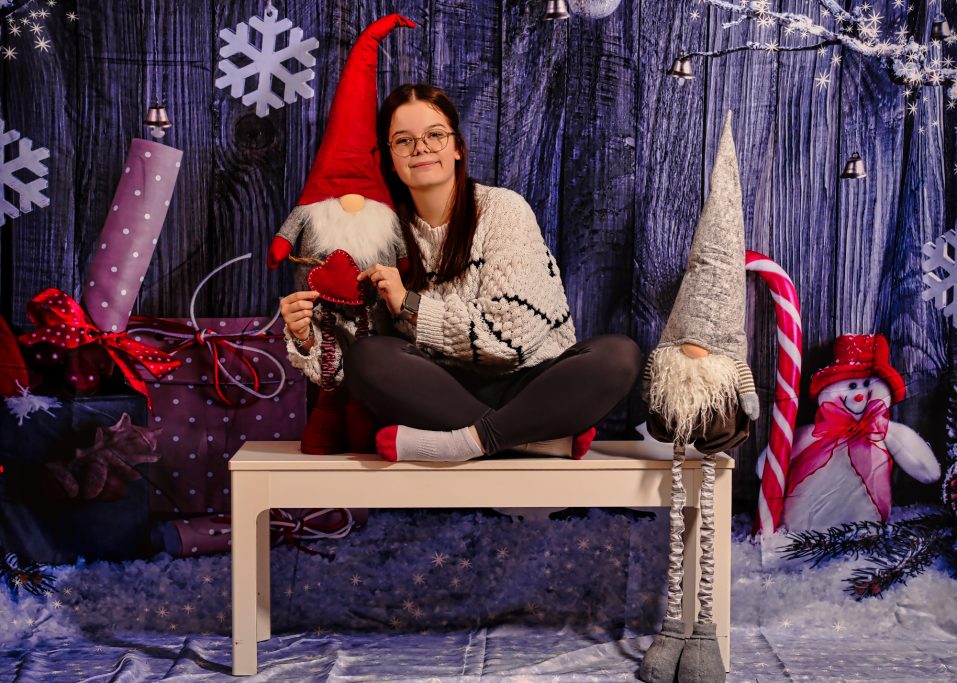 Frau sitzt auf einer Bank, umgeben von Weihnachtstrinket und zwei dekorativen Gnomen.